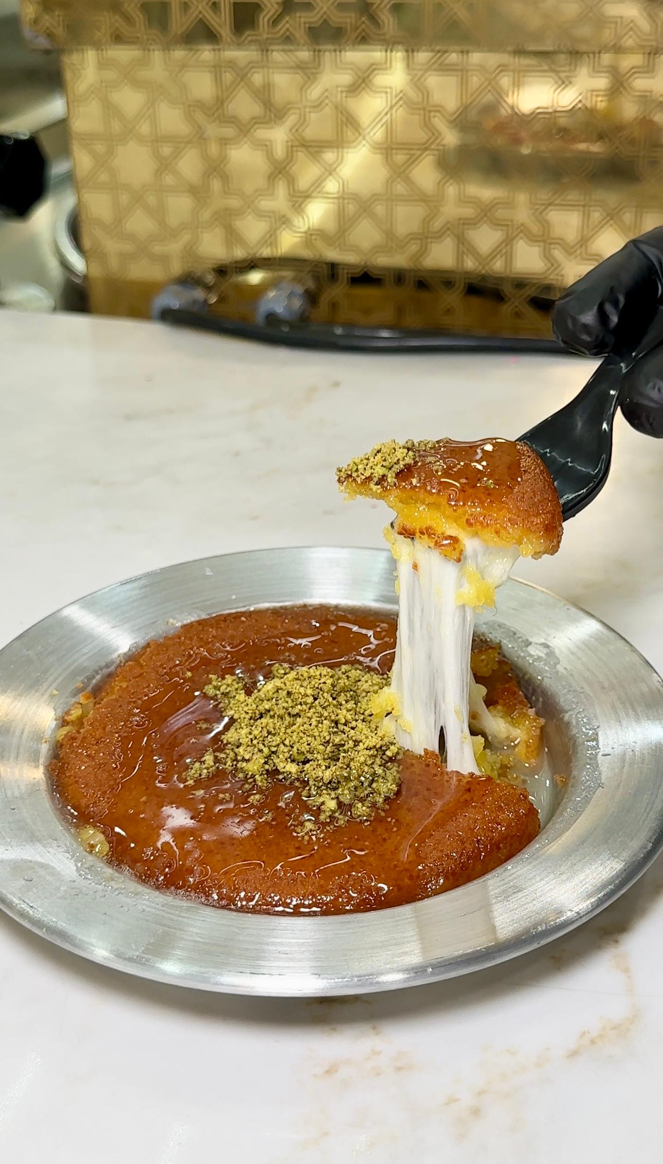 Traditional Kunafa with a golden crisp top, melted cheese pull, syrup, and ground pistachio garnish